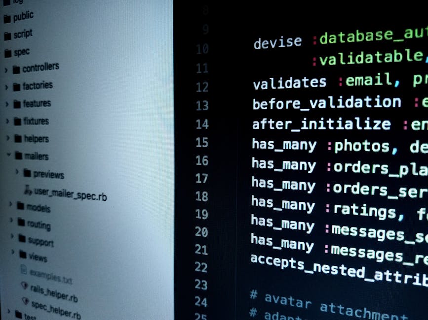 A close-up view of a laptop on a wooden desk displays lines of programming code on its dark screen, showing colorful syntax highlighting. Next to the laptop, there is a cream-colored ceramic mug with 